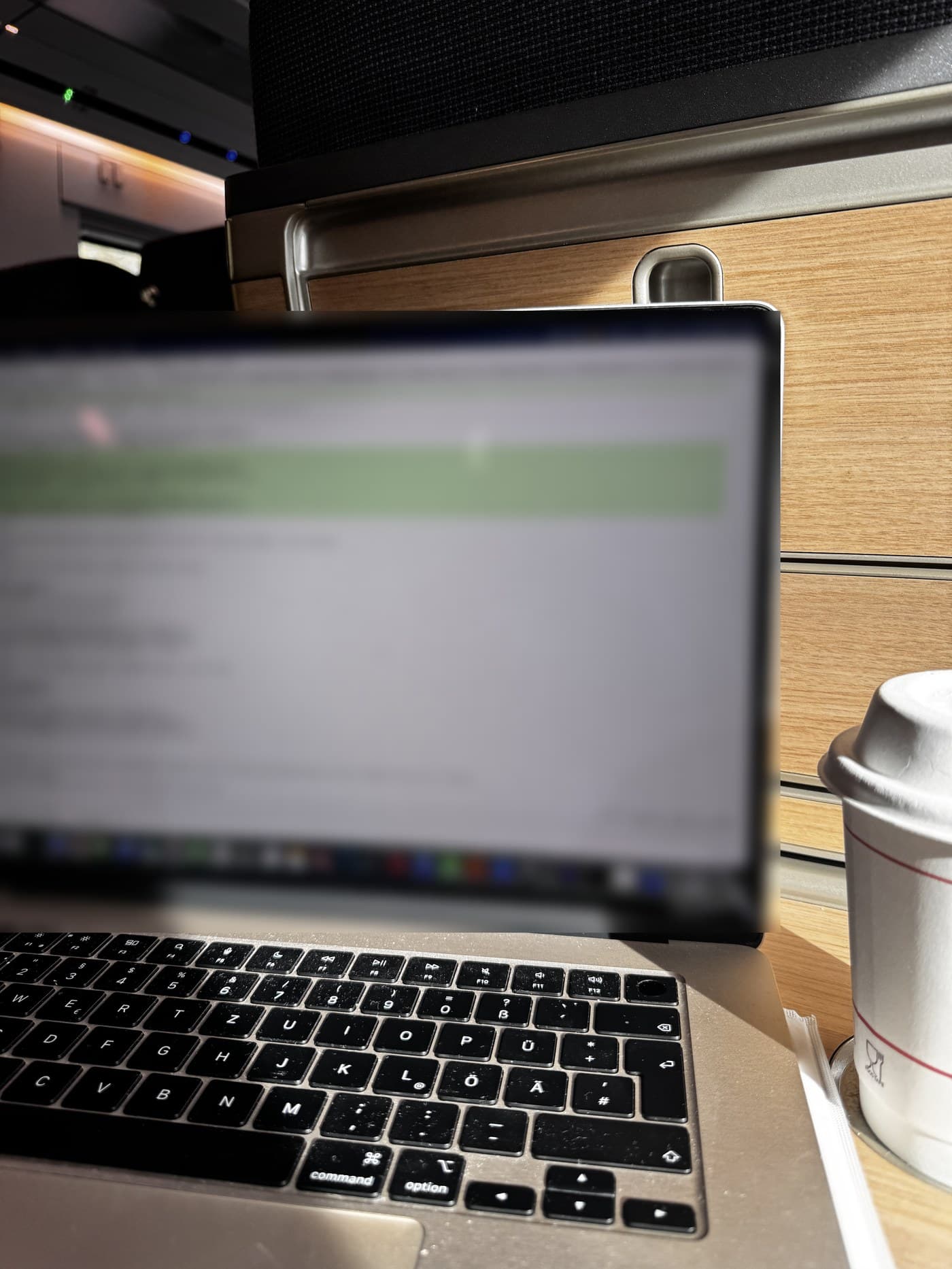 Laptop auf einem Klapptisch im Zug, daneben ein Kaffeebecher. Der Bildschirm ist unscharf.